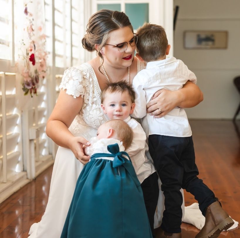 A Woman In A Wedding Dress Is Holding Two Children — Eternal Weddings & Couture In Woolner, NT