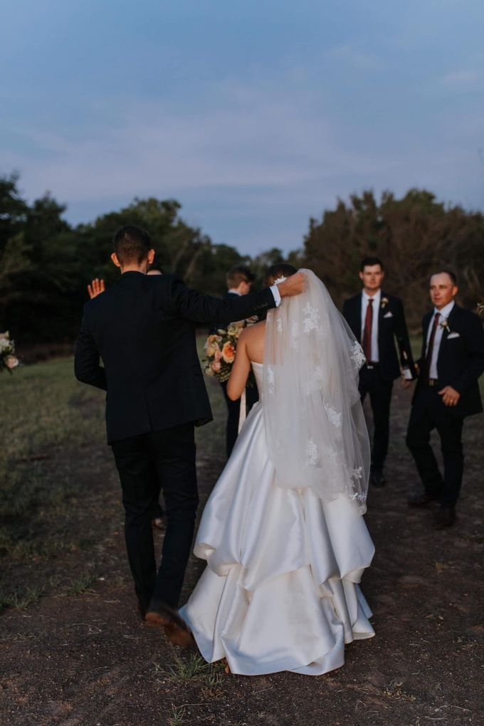 A Bride And Groom Are Walking Down A Dirt Road With Their Wedding Party — Eternal Weddings & Couture In Woolner, NT