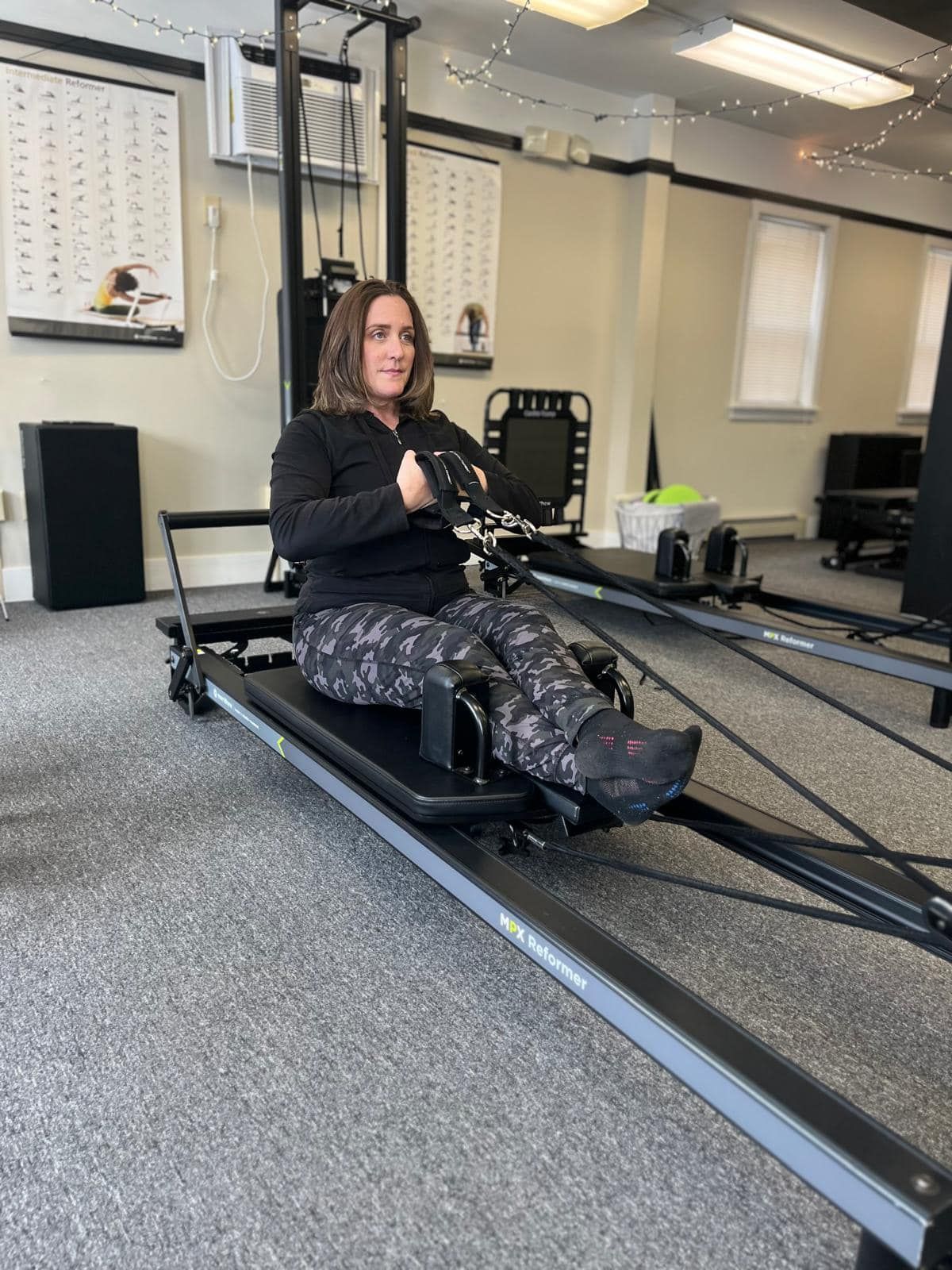 Woman using a Total Gym machine, pulling handles towards her chest, in a gym setting.