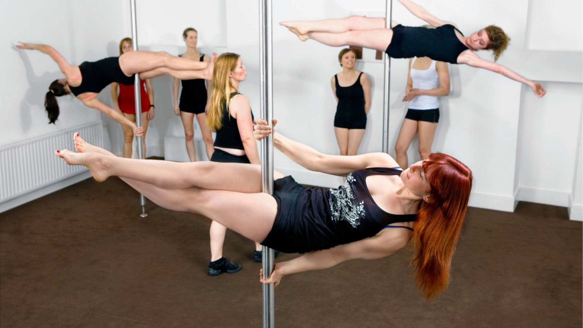 Women pole dancing in a studio, performing various poses on vertical poles.