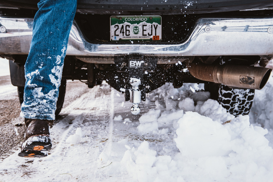 A person is standing on the back of a truck in the snow.