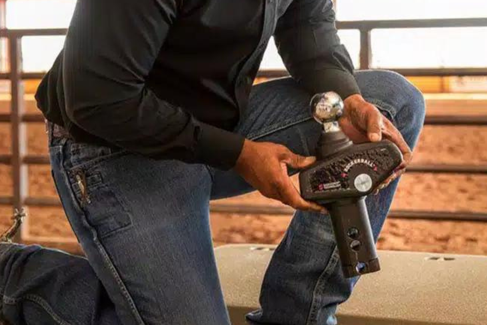 A man is kneeling down holding a trailer hitch.