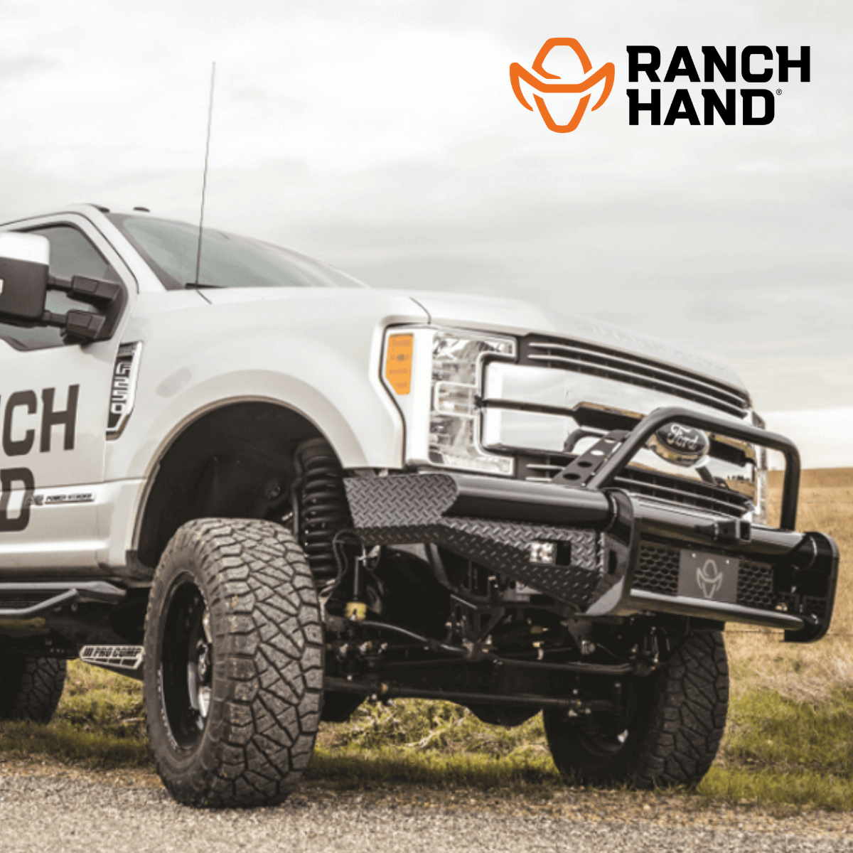 A white truck with the word ranch hand on the side is parked on a dirt road.