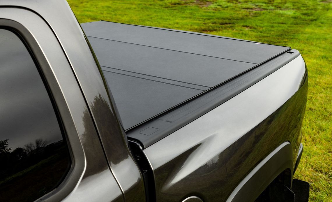 A truck with a black tonneau cover is parked in a grassy field.