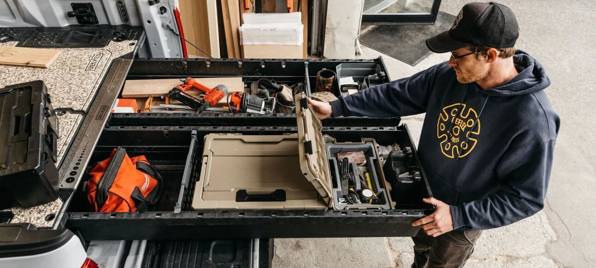 A man is standing in a garage holding a toolbox.