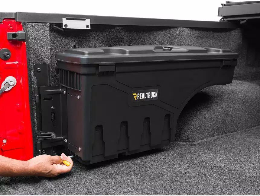 A person is holding a wrench next to a toolbox in a truck bed.