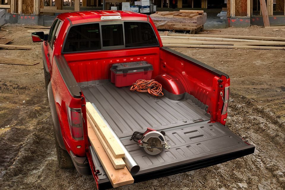 A red truck is parked in a construction site with its bed open.