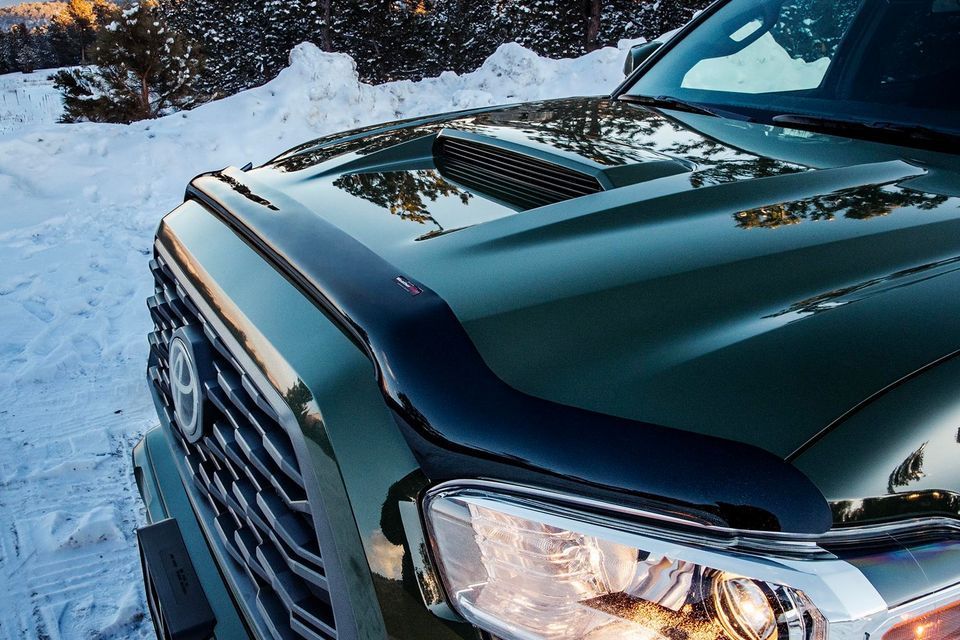 A green truck is parked in the snow with the hood up