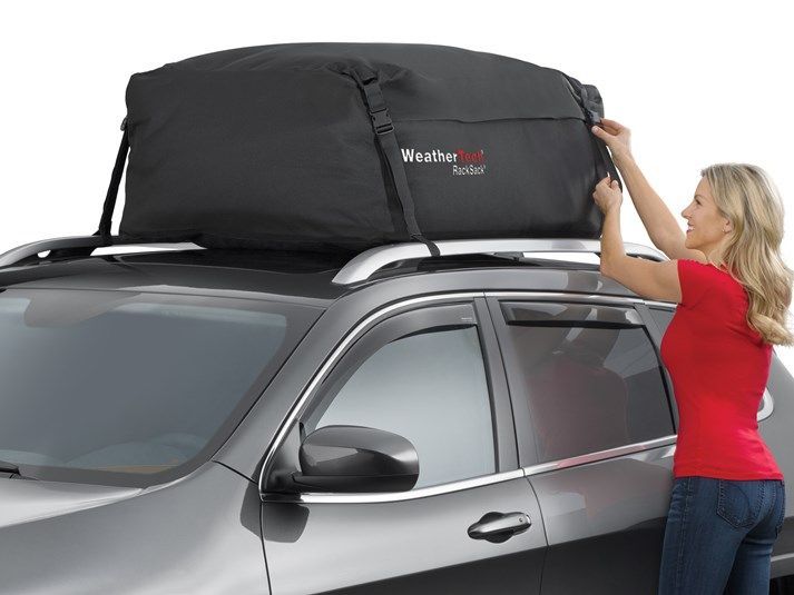 A woman is putting a roof bag on top of a car.