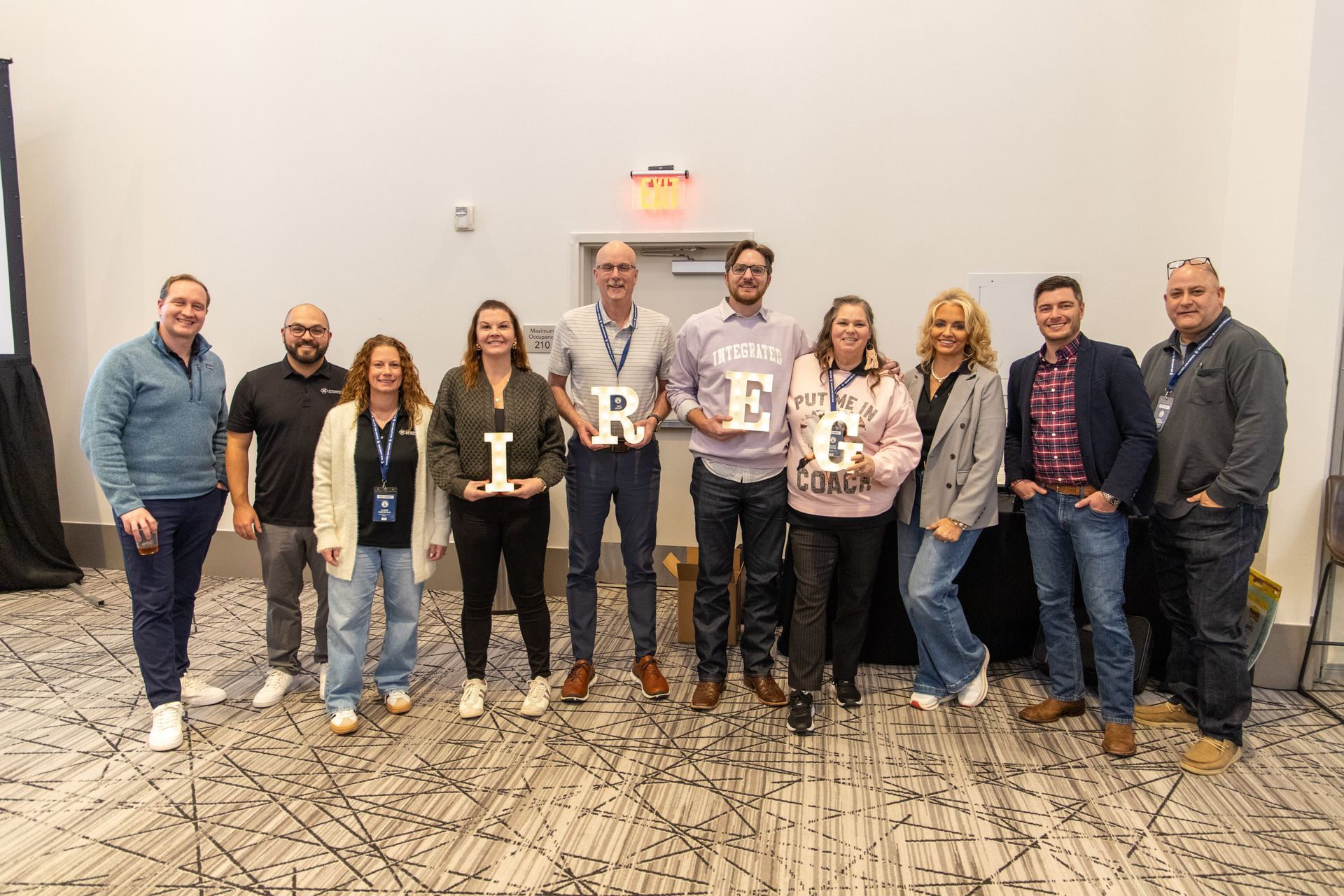 A group of eleven adults standing in a line, holding letters that spell 