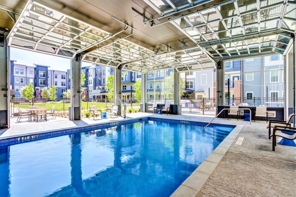 Indoor swimming pool with open glass garage-style doors leading to an outdoor patio in an apartment complex.