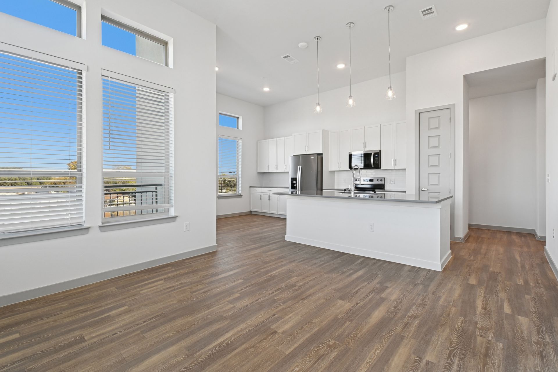 A bright, modern kitchen featuring white cabinets, stainless steel appliances, an island, and light wood-look flooring.