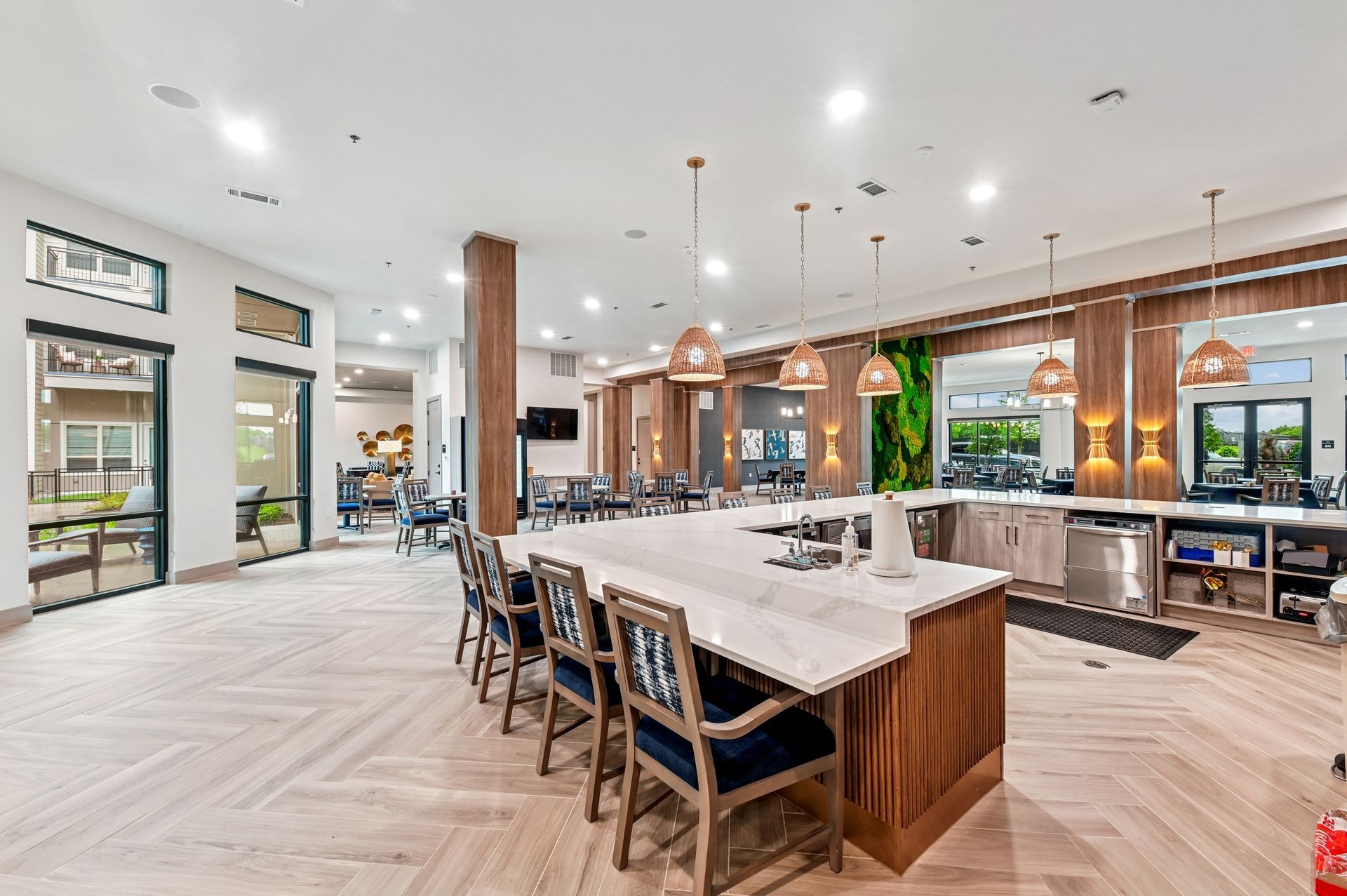 Modern apartment community lounge with a kitchen island, bar seating, wood flooring, and large windows.