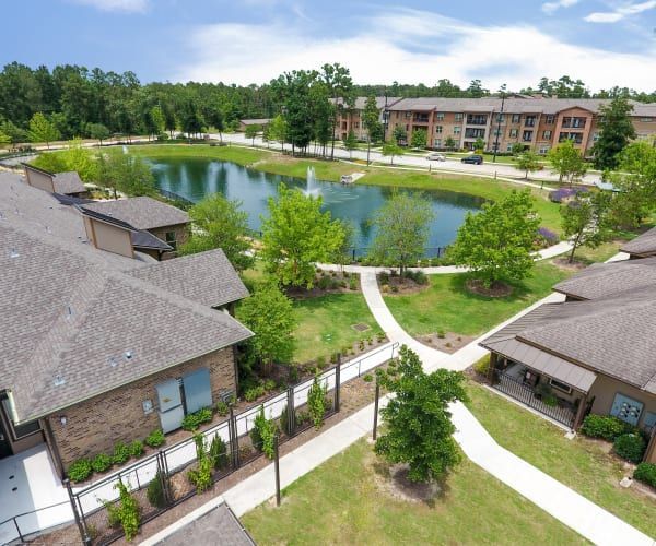 An aerial view of an apartment complex with brick buildings, walkways, green lawns, and a fountain in a central pond.