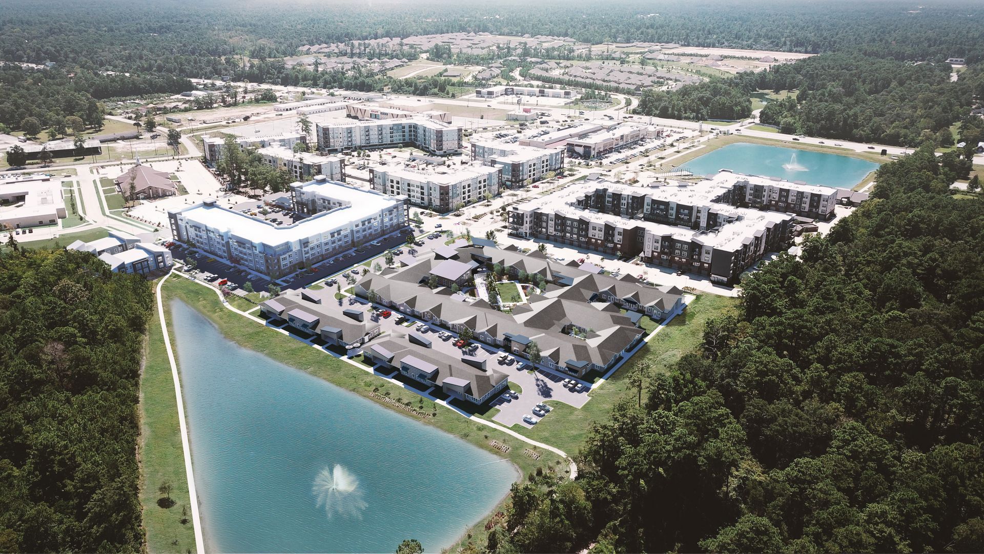 Aerial view of a residential complex with multiple buildings, parking areas, and two ponds surrounded by forest.