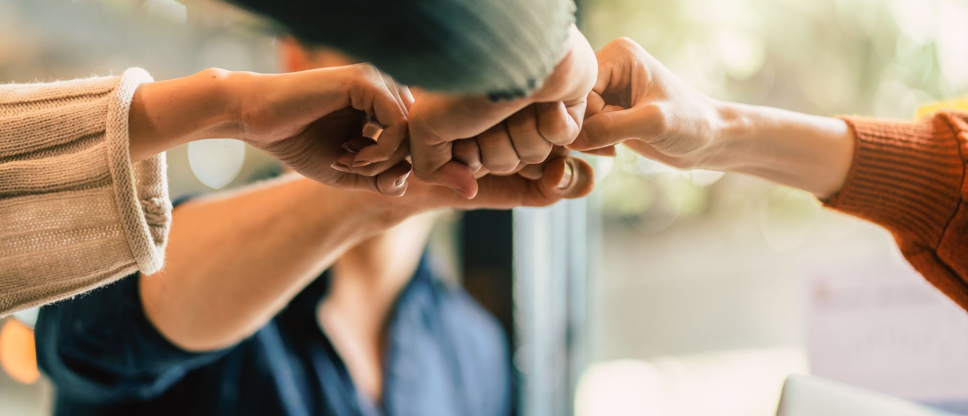 Three people's hands meet in the center to perform a fist bump, symbolizing unity, collaboration, and teamwork.