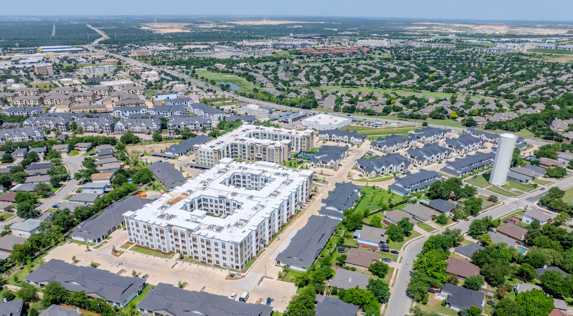 Aerial view of a large apartment complex surrounded by suburban neighborhoods and a water tower on a sunny day.
