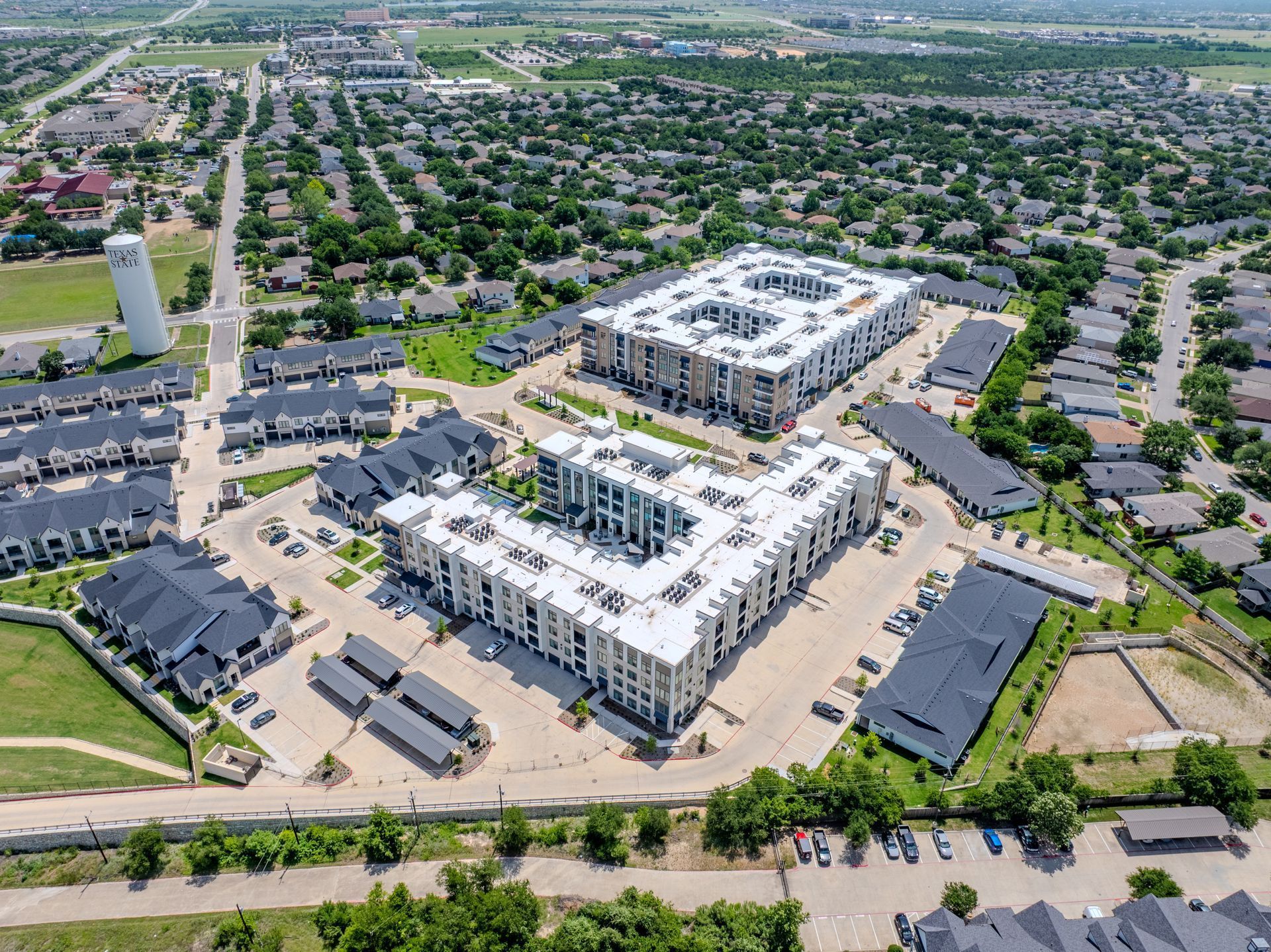 Aerial view of a modern apartment complex with multiple U-shaped buildings surrounded by suburban homes and green spaces.