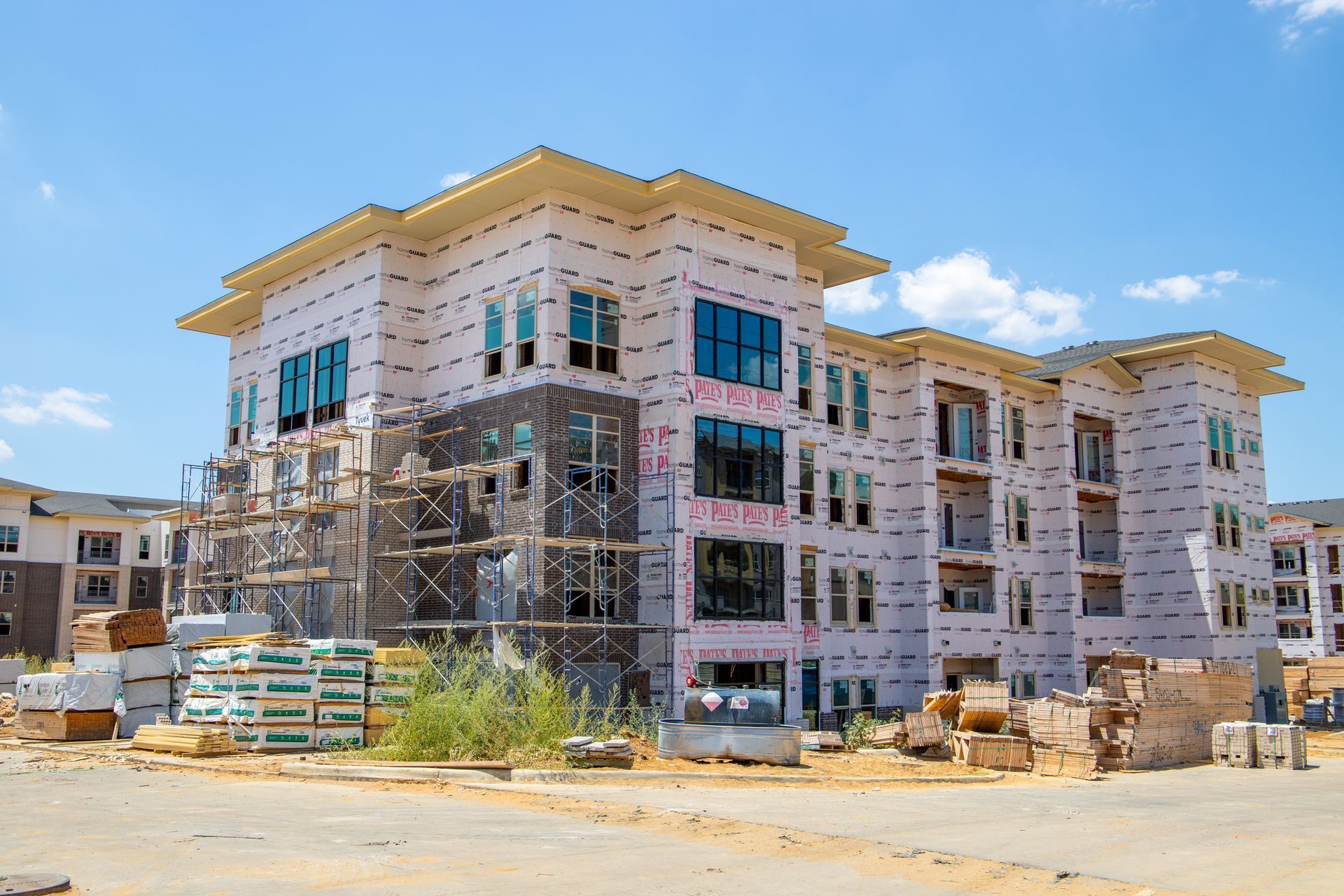 A large, multi-story apartment building under construction, featuring white sheathing and dark window frames.