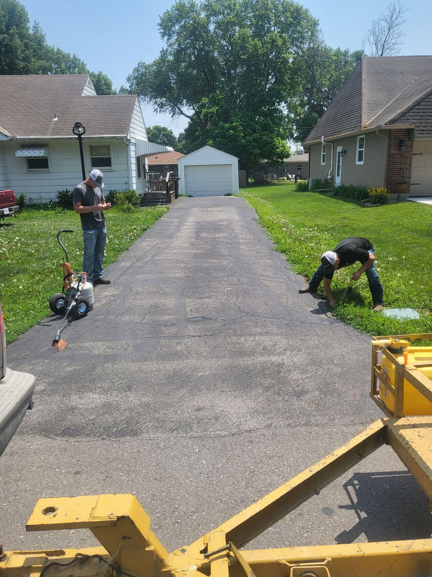 Two men are working on a driveway in front of a house.