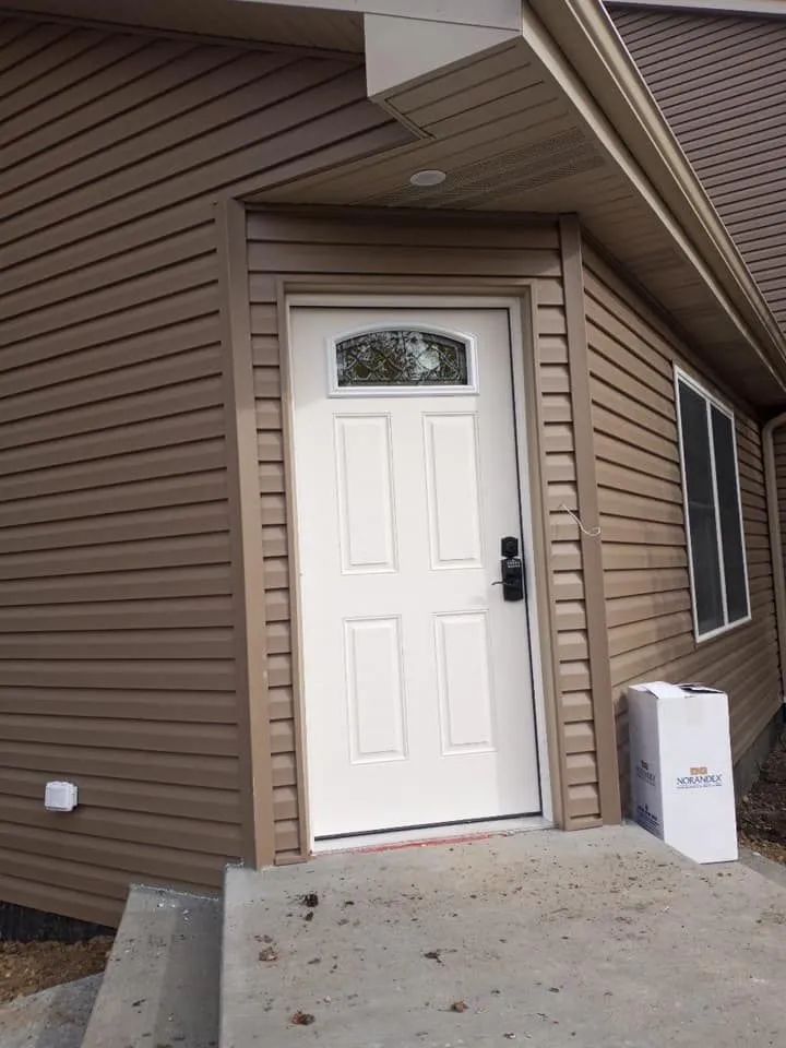 Front entrance of a house with a white door, tan siding, and a concrete walkway.