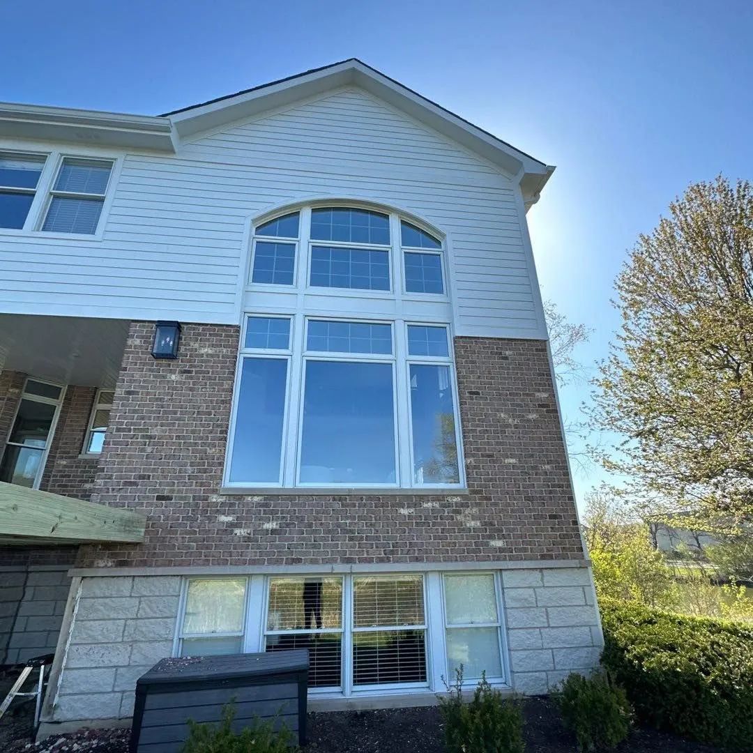 A two-story house with a large arched window. Brick and white siding. Sunny sky.