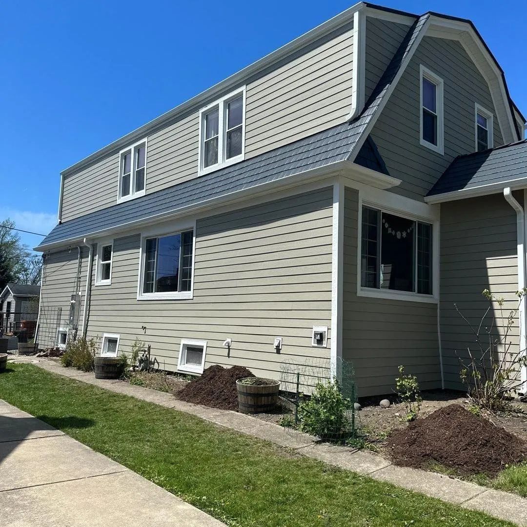 Two-story house with green siding, a gray roof, and white window frames under a clear blue sky.