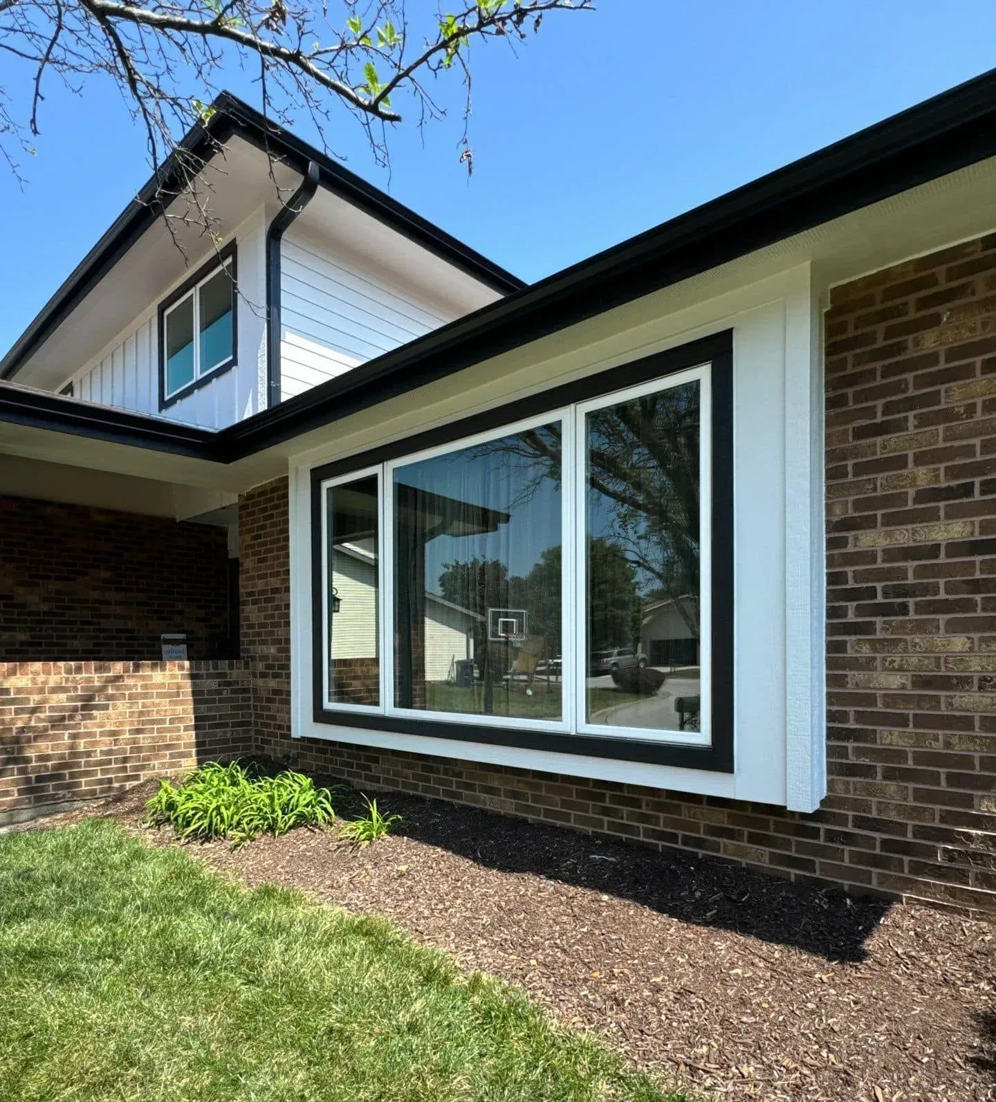 Modern house exterior with brick walls, white trim, and a large bay window over mulch and grass