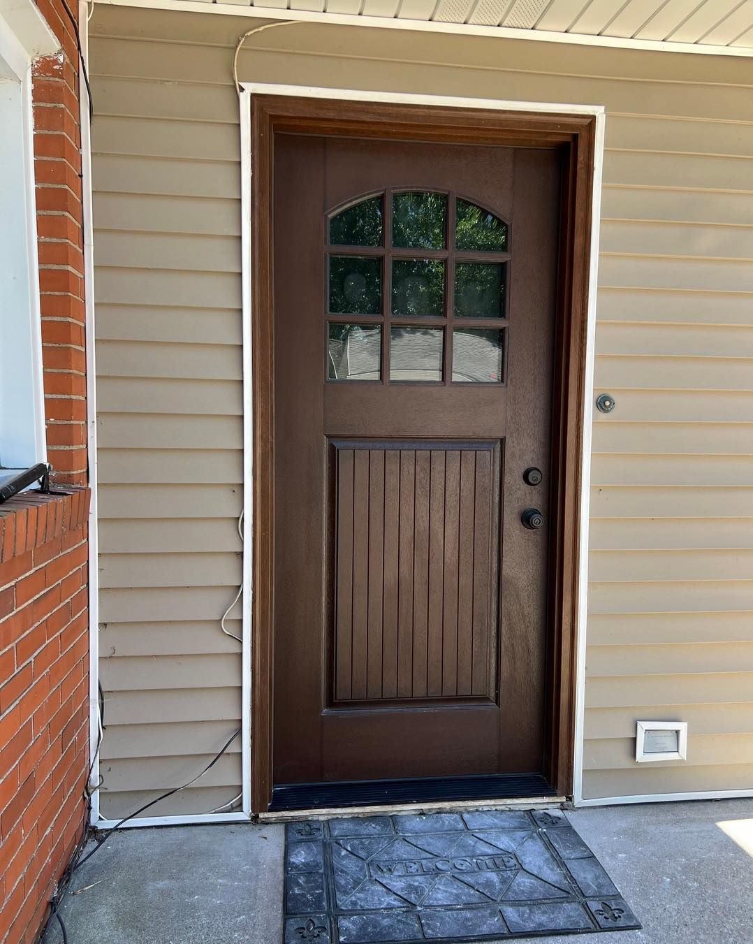 Gray house with porch and steps, tan door, white railing, and a black light fixture.