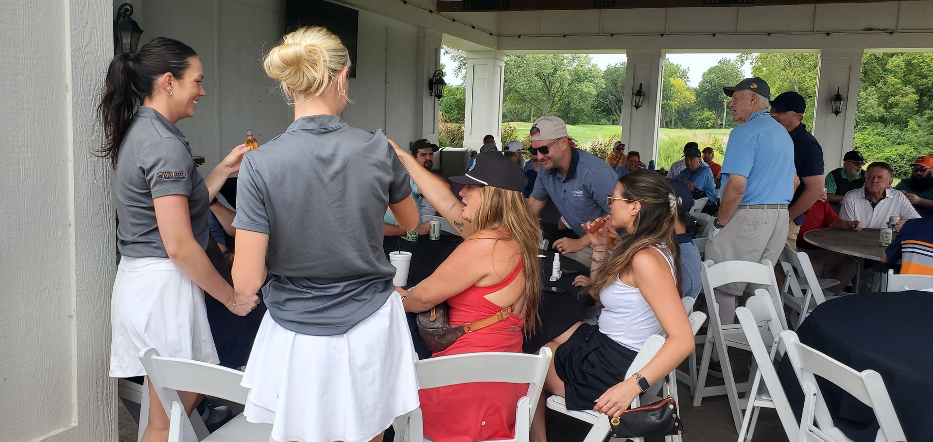 People socializing under a pavilion, with women in golf attire and others wearing casual clothes.