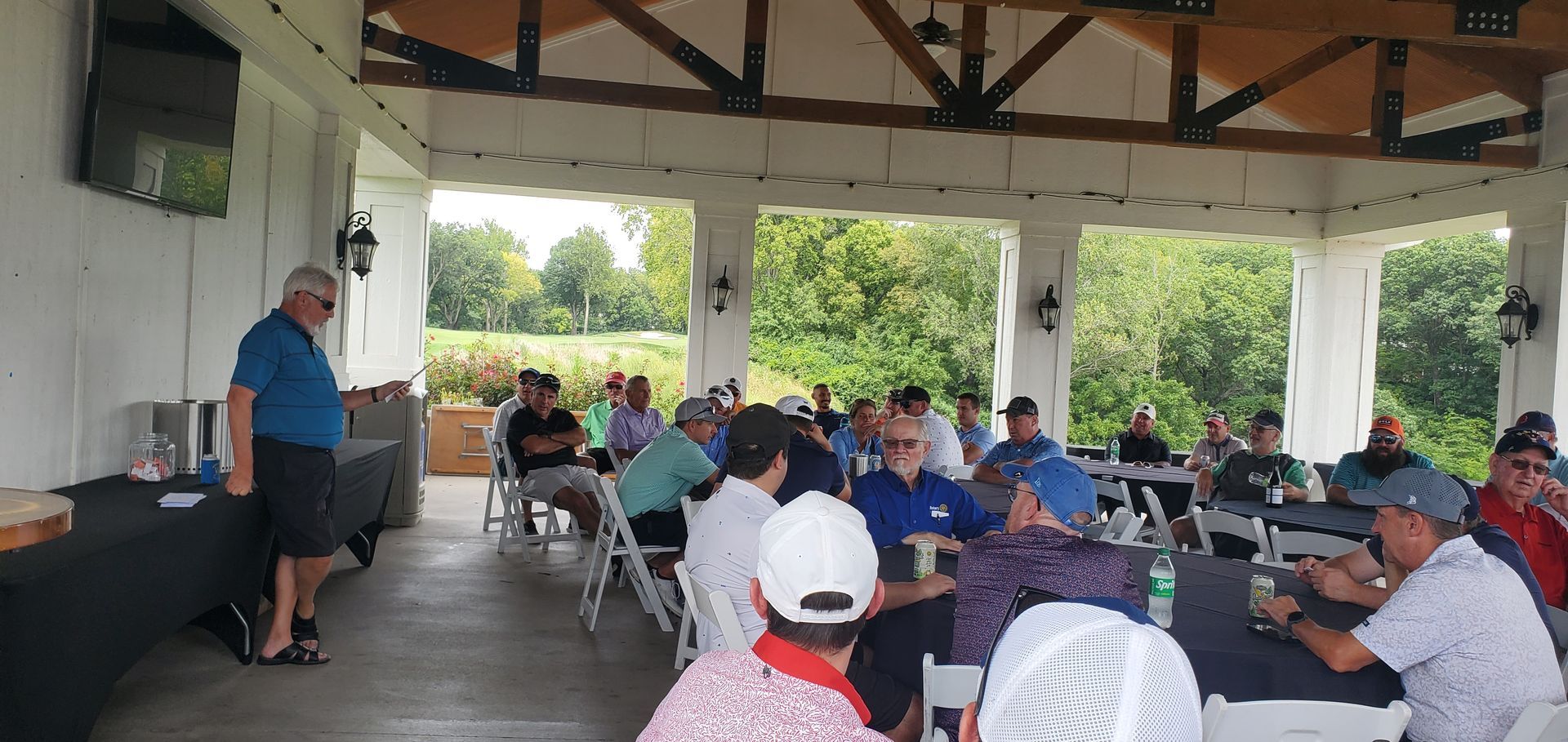 Group of people gathered under a pavilion for a presentation at a golf course.