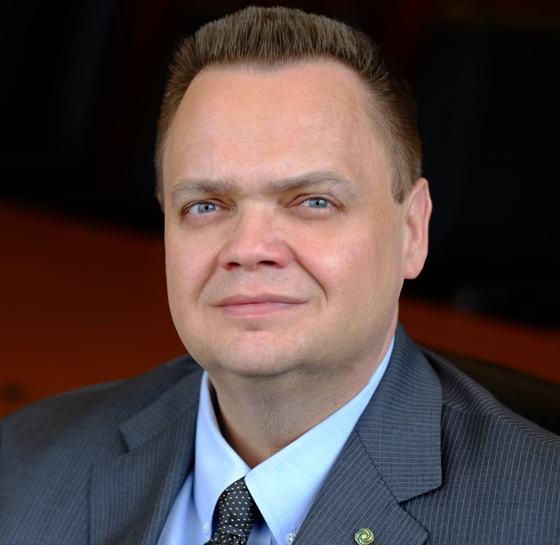 A middle-aged man with short brown hair in a suit smiles.
