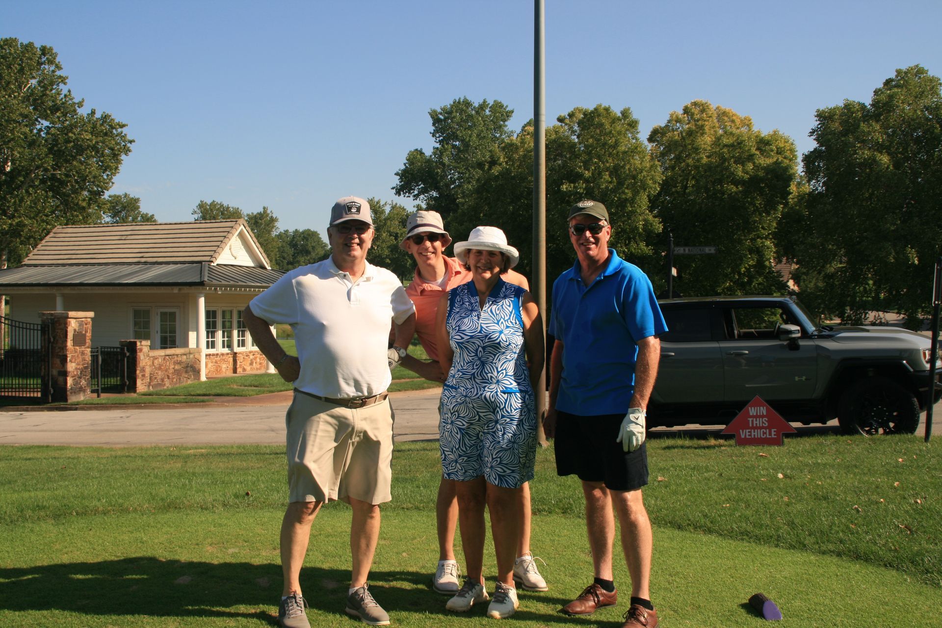 Four golfers smiling on a green. A flagpole is in the center, and a Bronco is behind them.