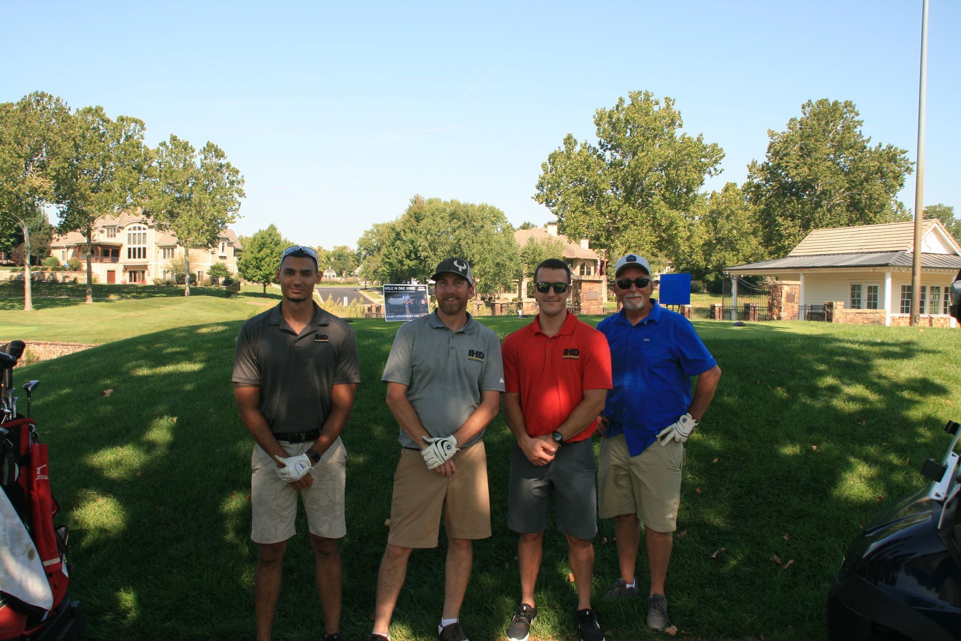 Four men in golf attire pose on a sunny golf course.