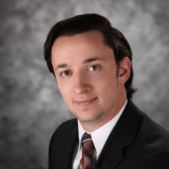 Man in suit smiling, professional portrait on a neutral background.