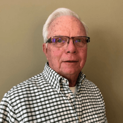 Older man with white hair and glasses smiles, wearing a black and white checkered shirt.