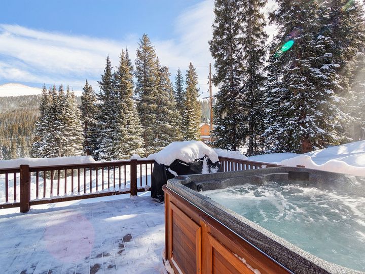A hot tub on a snowy deck with trees in the background