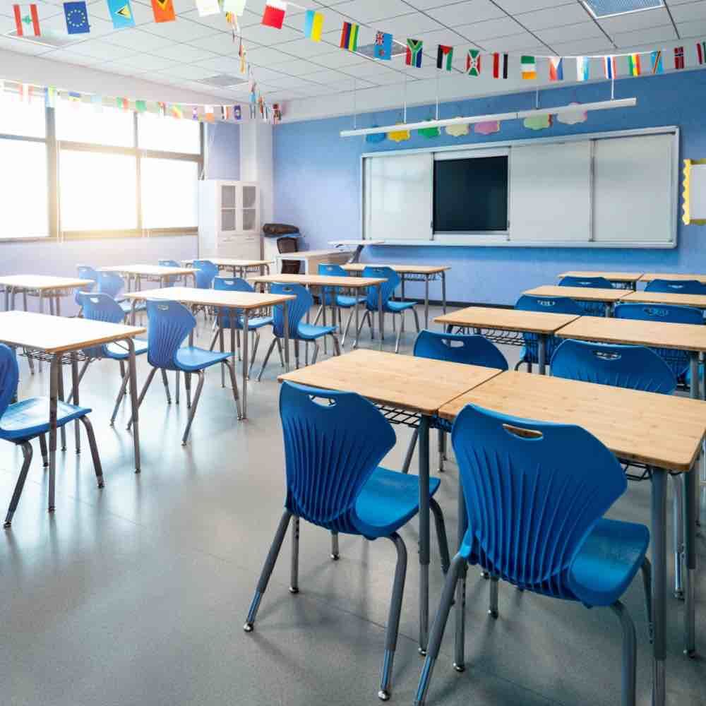 Clean classroom with blue chairs, wooden desks, and international flags.