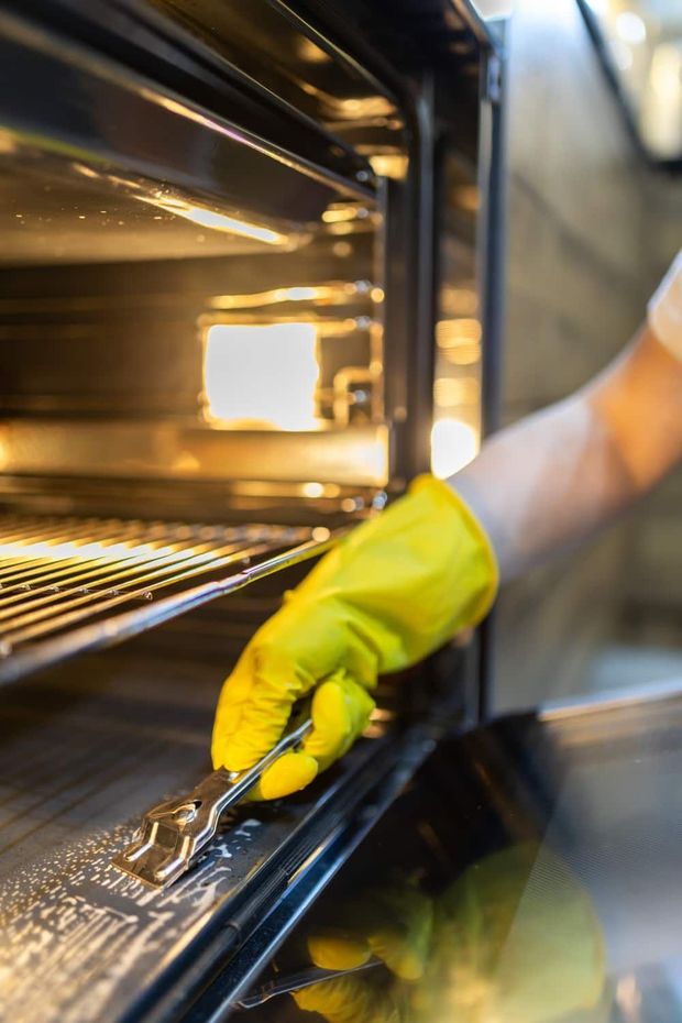 Person in yellow glove cleans oven with scraper.