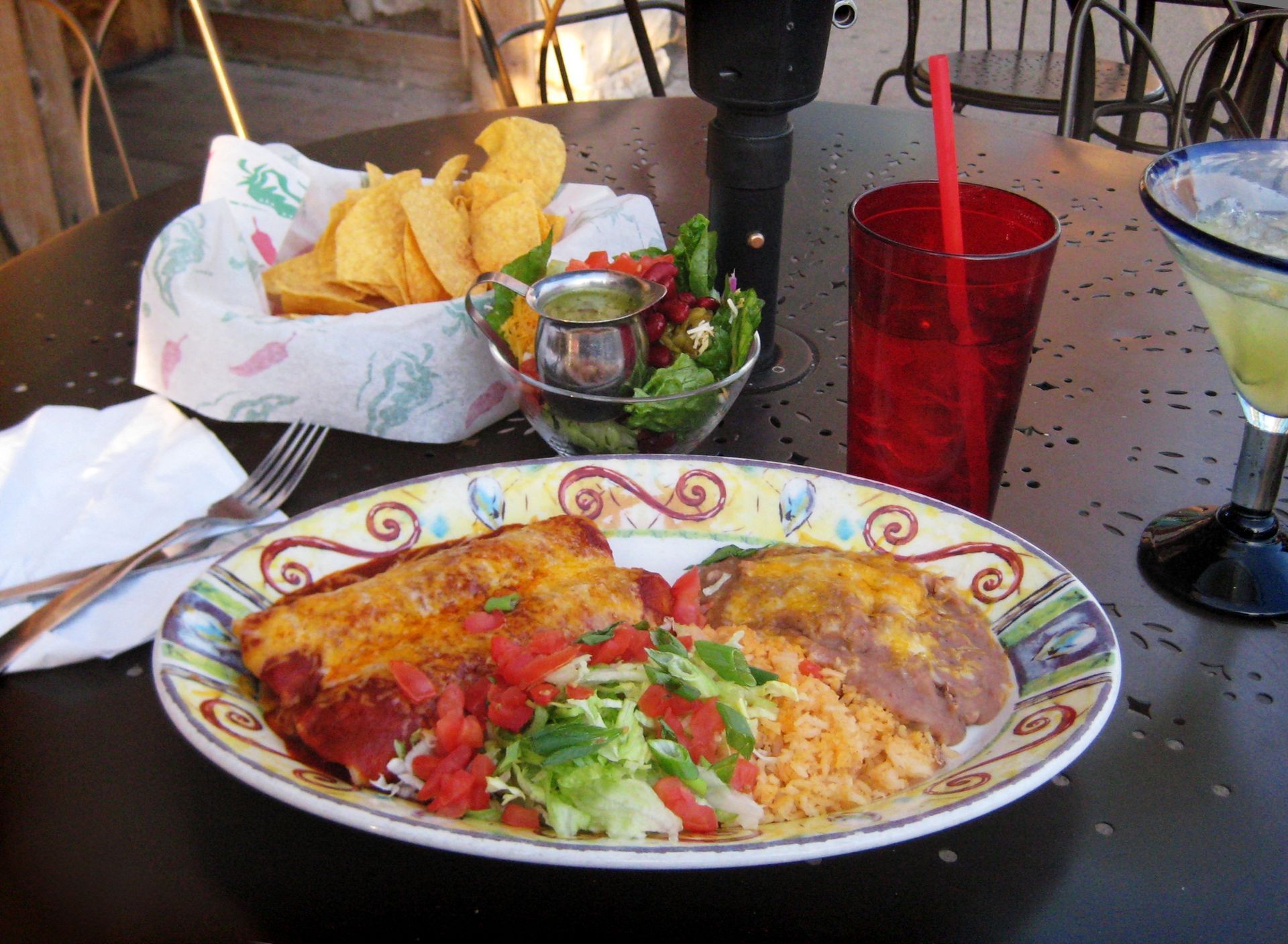 Mexican meal on a patterned plate with chips, salsa, salad, and red drink on an outdoor table
