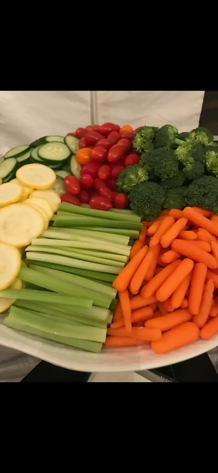 Assorted fresh chopped vegetables arranged on a platter, including carrots, cucumbers, broccoli, cherry tomatoes, zucchini, and celery.