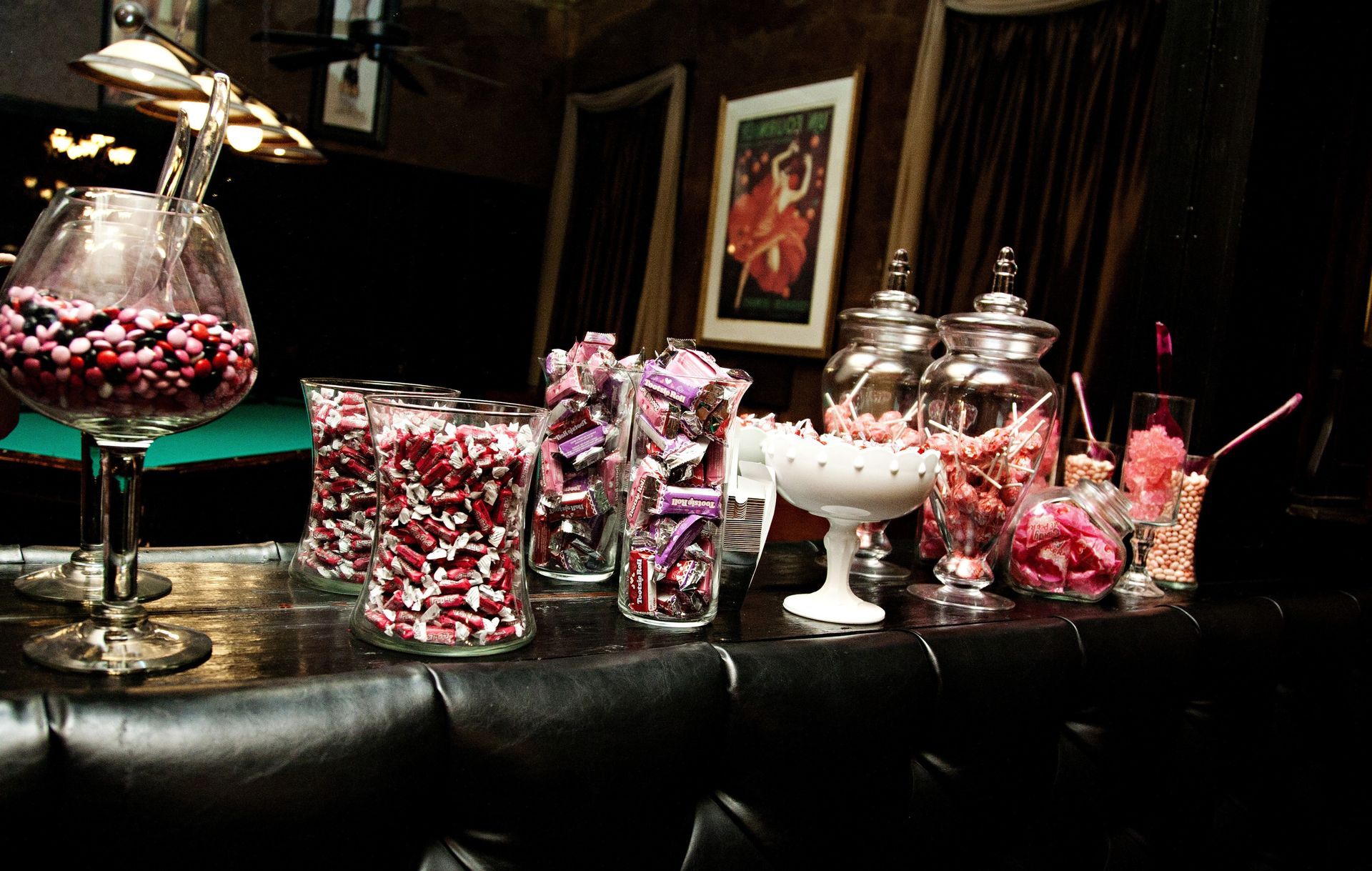Candy buffet with glass jars of pink and white sweets on a dark table.