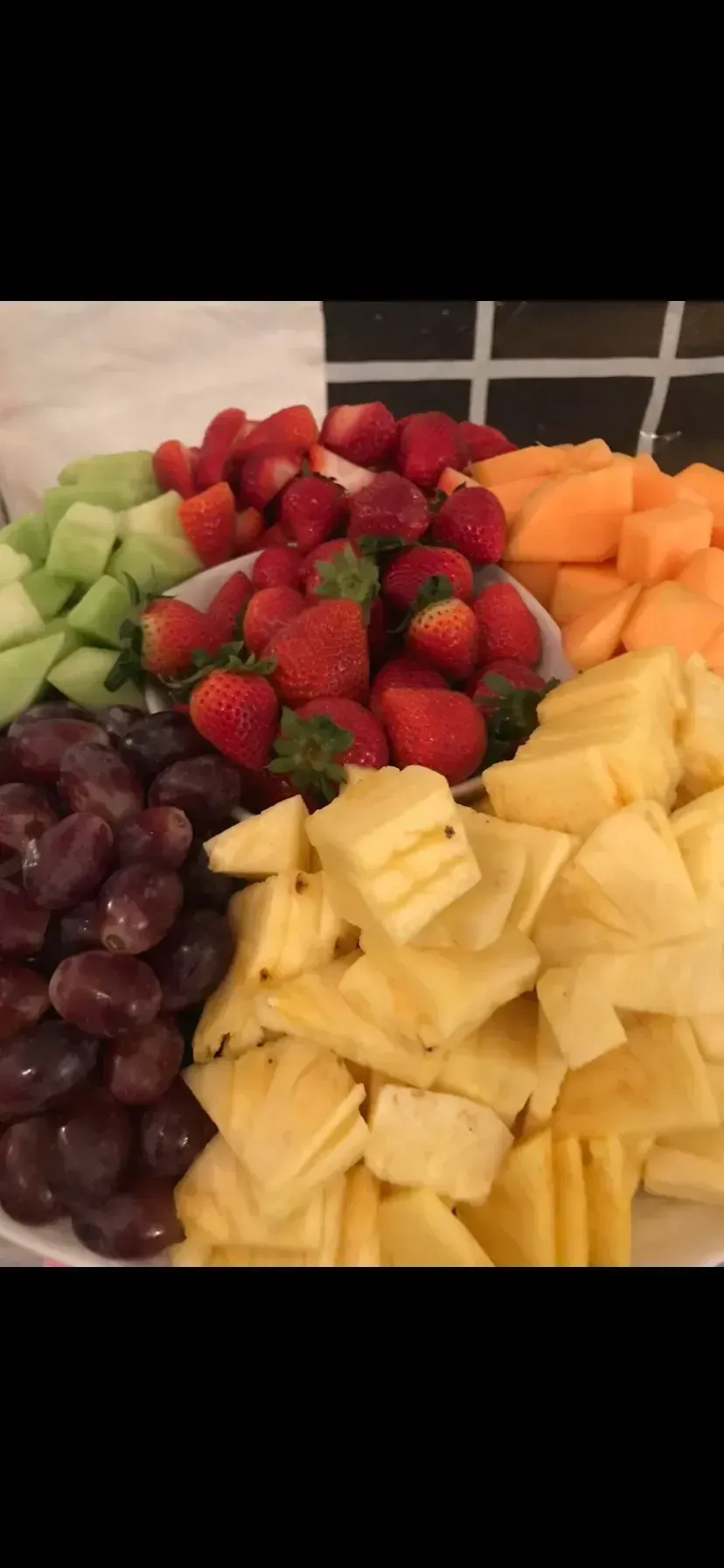 Assorted fresh fruit arranged in sections, including strawberries, grapes, pineapple, cantaloupe, and honeydew.
