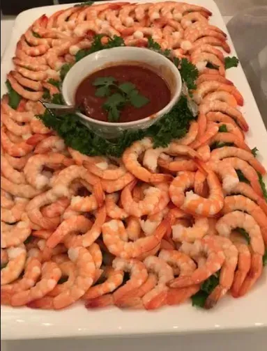 Platter of shrimp arranged around a bowl of cocktail sauce, garnished with parsley.