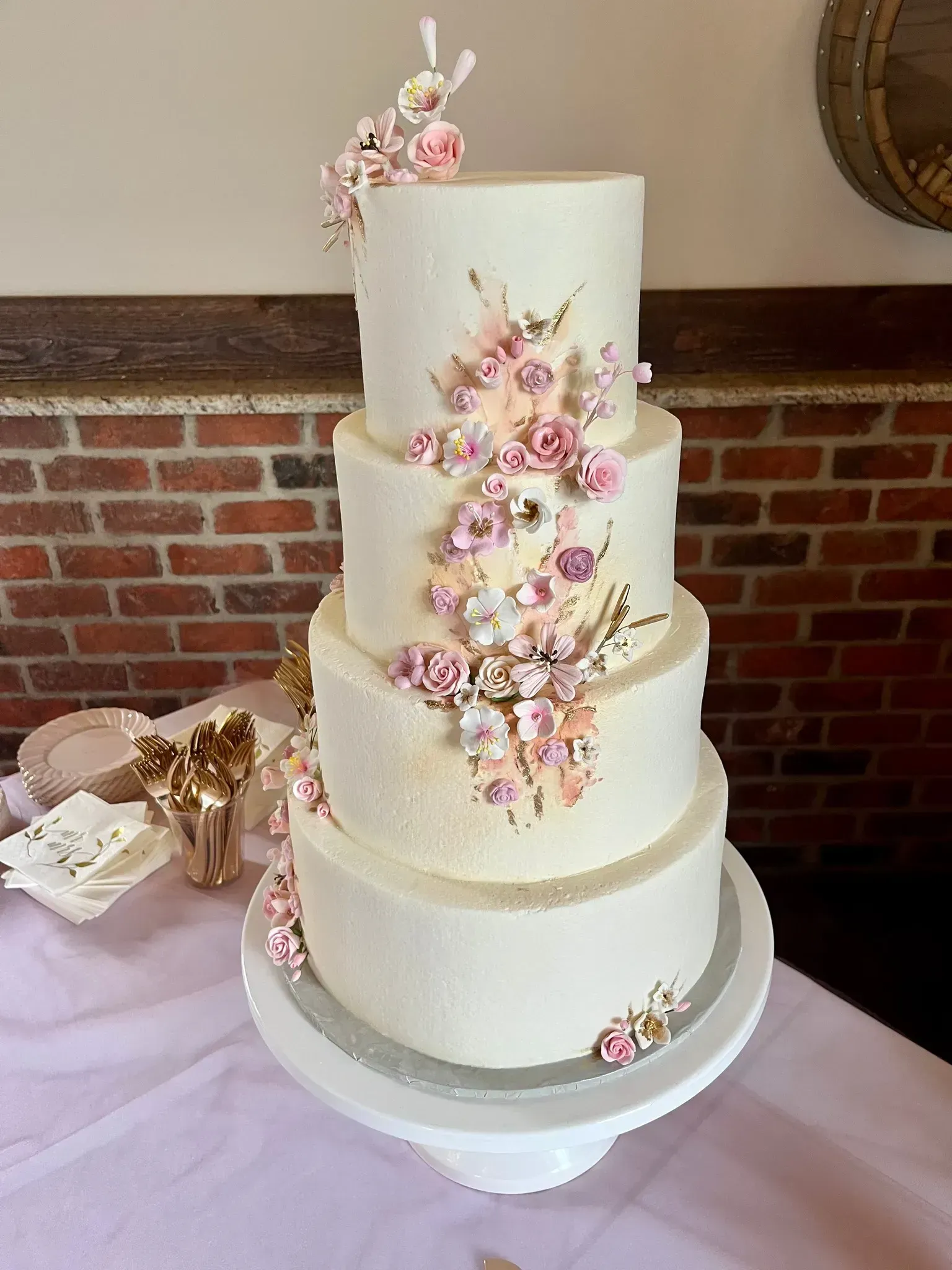 Three-tier white wedding cake with pink floral decorations on a table indoors