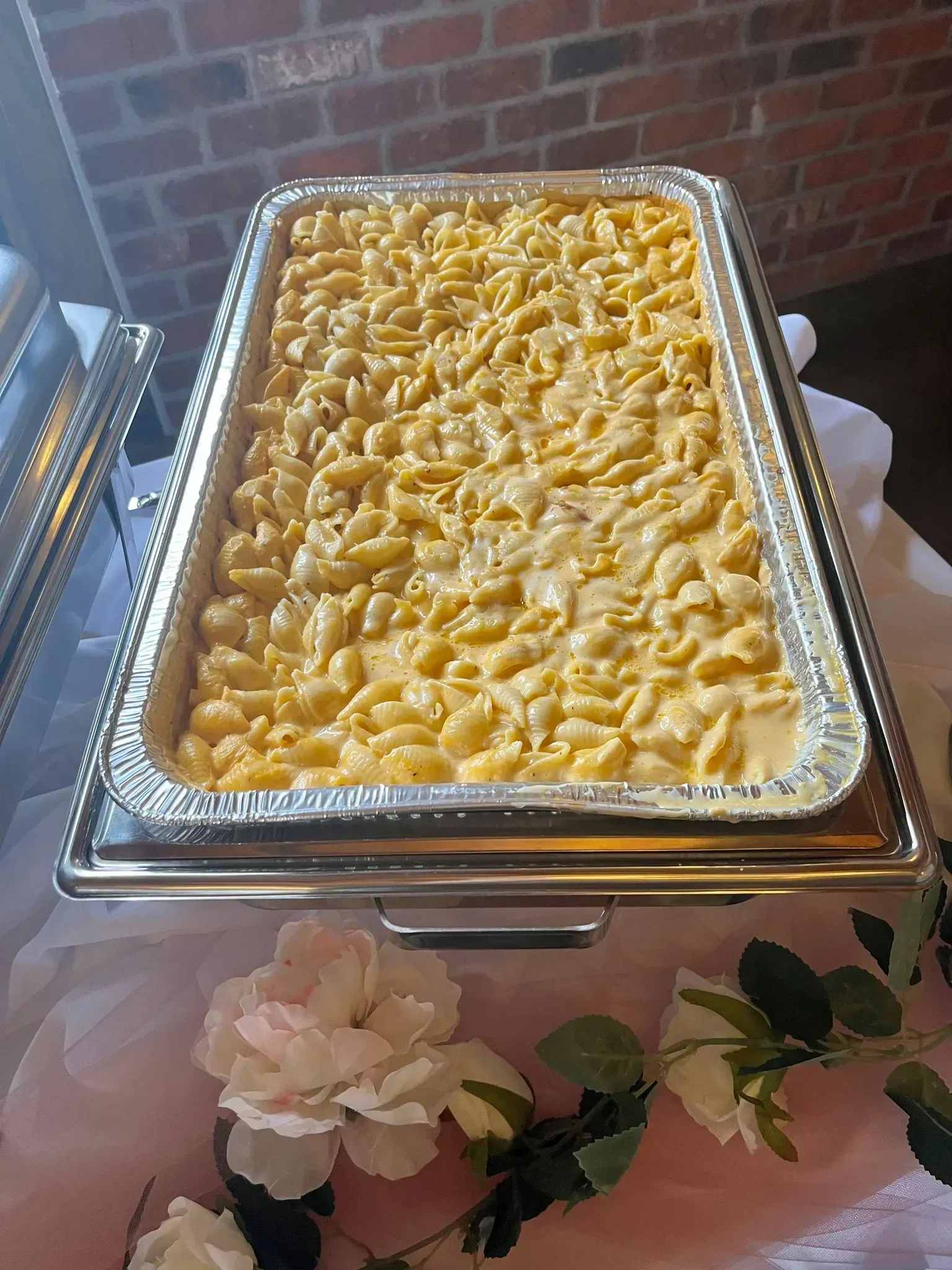 Tray of creamy macaroni and cheese in a buffet chafing dish, with floral decorations nearby