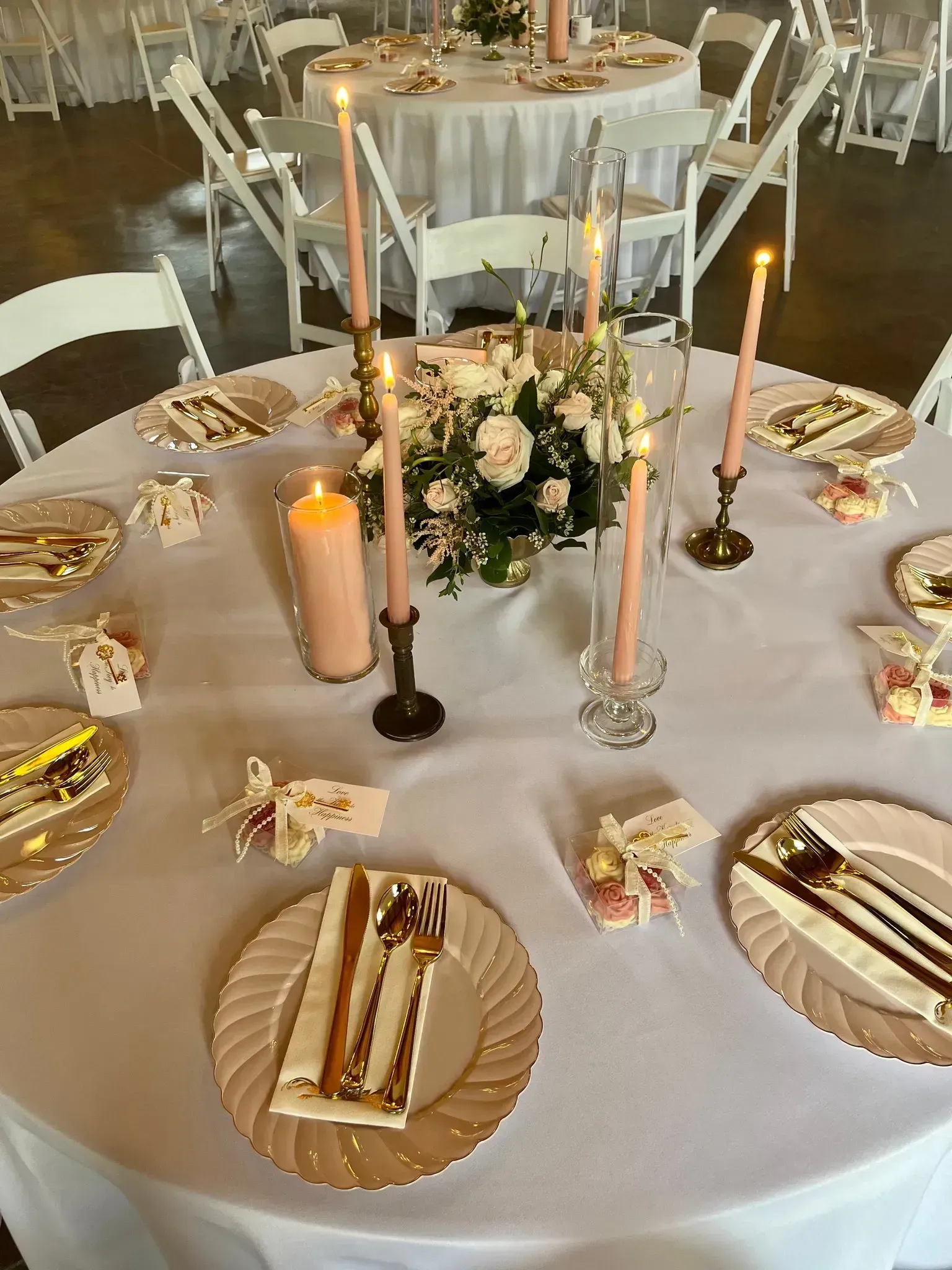 Elegant banquet table with white linens, gold accents, floral centerpiece, and lit candles