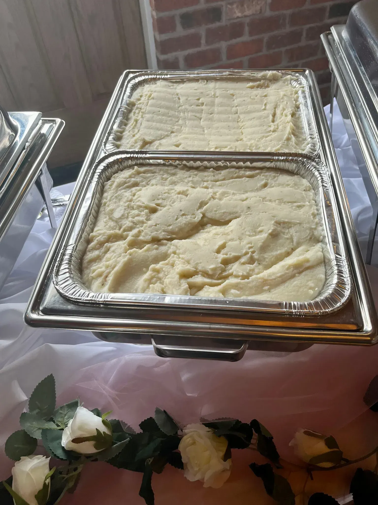 Chafing dish of mashed potatoes at a buffet, with floral garland along the table edge.