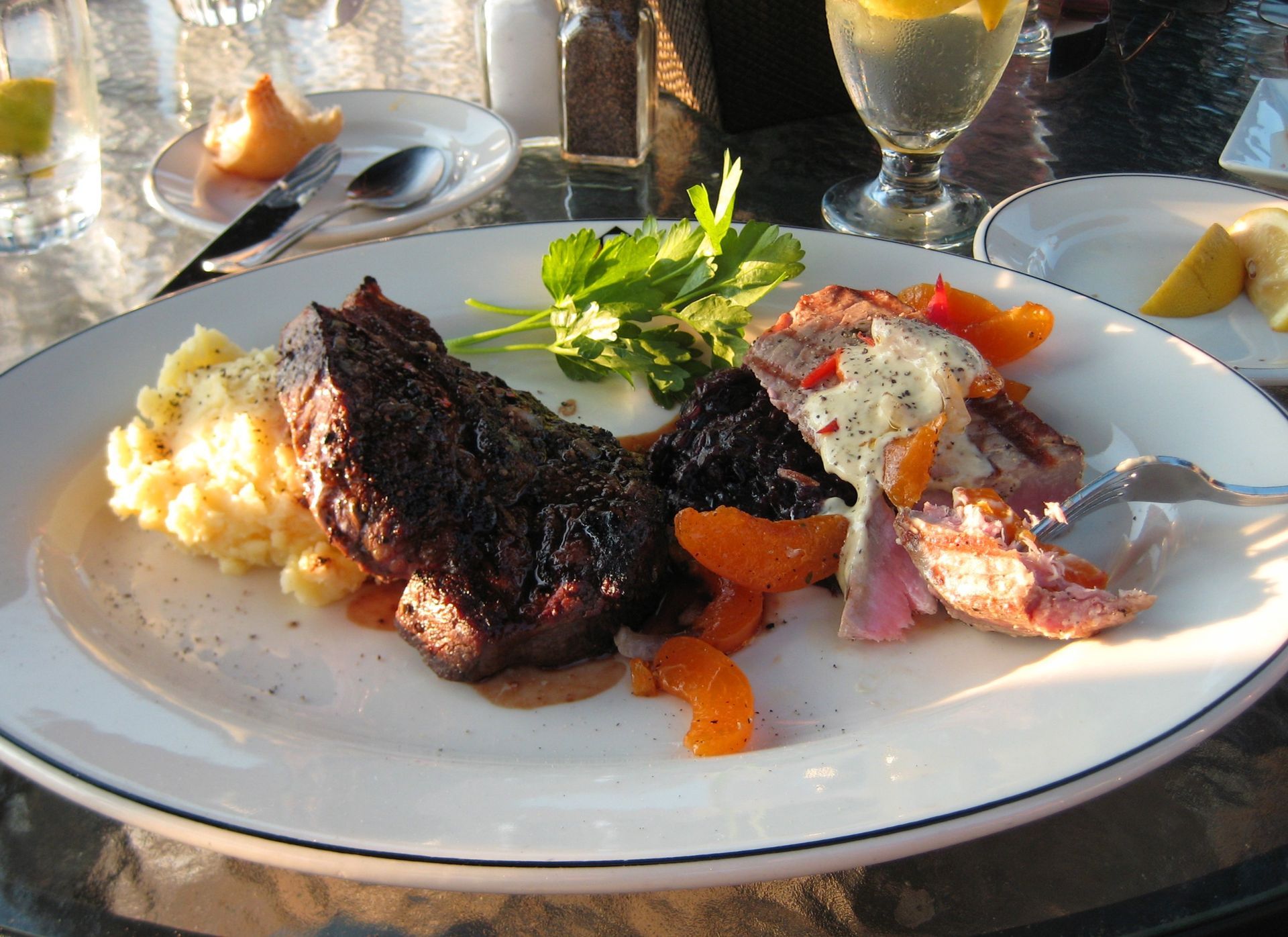 Grilled steak with vegetables and mashed potatoes on a white plate at an outdoor table