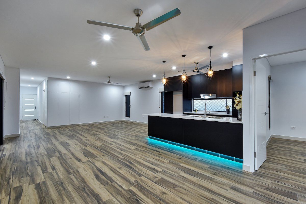 A large empty room with a kitchen and a ceiling fan.